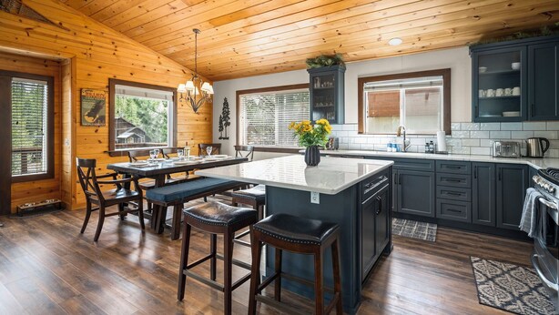 A spacious kitchen with wooden ceiling, a central island, bar stools, and a dining area. - Pet-Friendly Escape | Hot Tub, King Suite, Rec Center Access | Near Lake, Trails (Truckee)