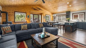 A cozy cabin interior with a wooden ceiling, a sectional sofa, a dining area, and a kitchen with wooden cabinets. - Pet-Friendly Escape | Hot Tub, King Suite, Rec Center Access | Near Lake, Trails (Truckee)