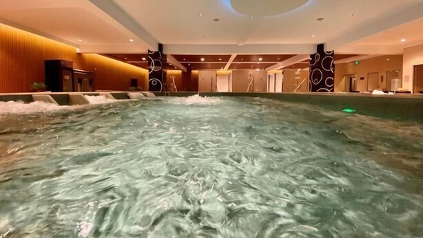 A large indoor pool with water jets, a circular ceiling light, and a modern interior design. - Huasheng Holiday Hotel (Kaiping)