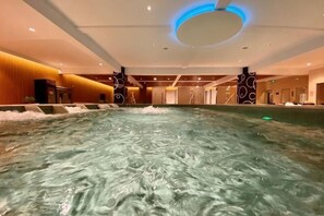 En stor inomhuspool med vattenstrålar, en rund taklampa och en modern inredningsstil.