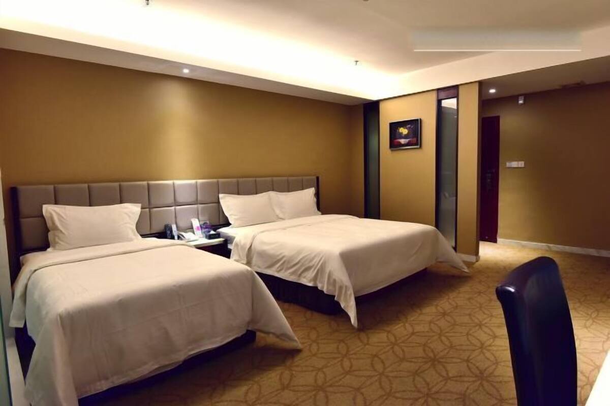 A hotel room with two beds, a nightstand, a chair, and a door leading to another room.