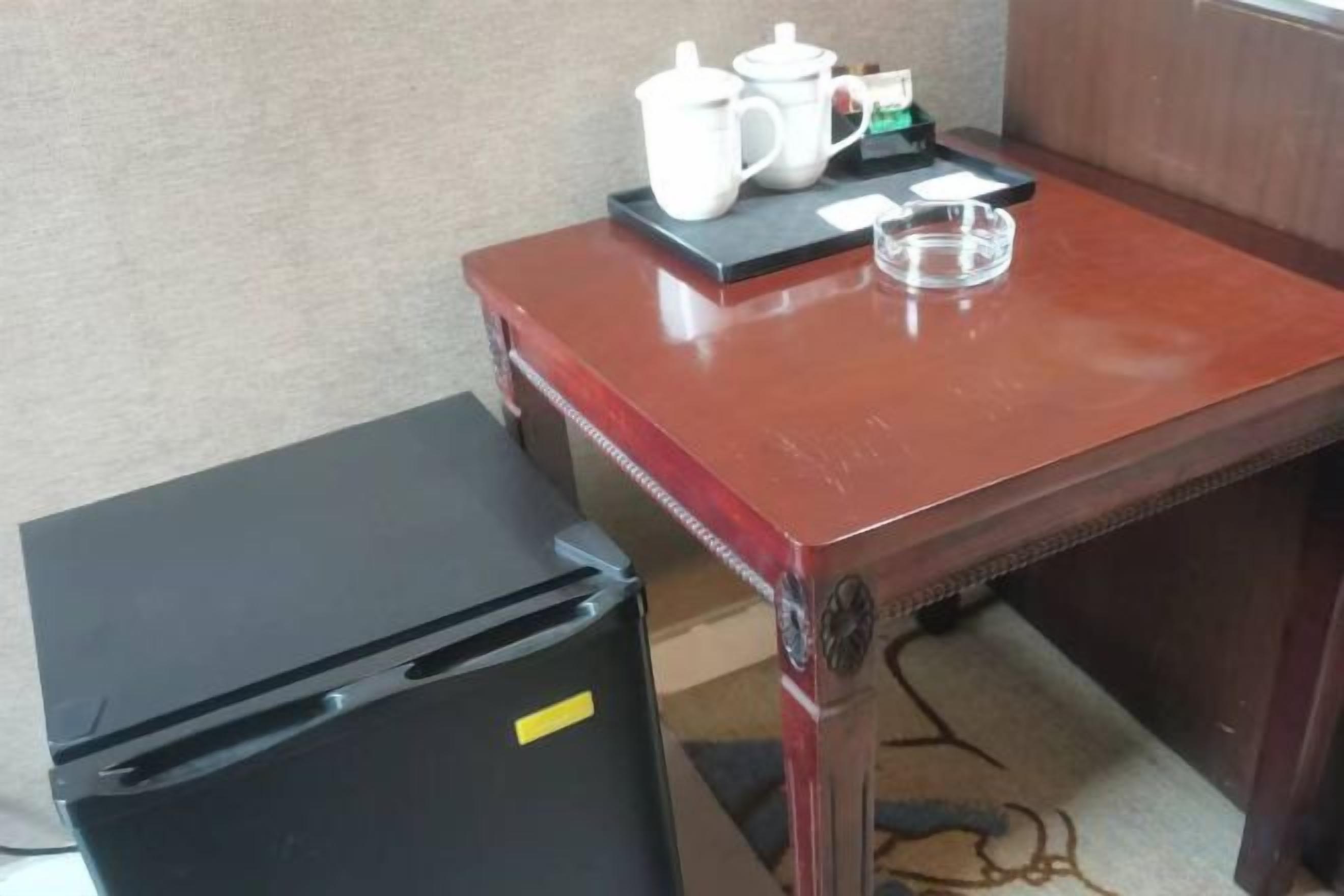 Un petit coin cuisine comprenant un réfrigérateur, une table en bois sur laquelle se trouve un plateau avec une théière, une tasse et un petit bol.