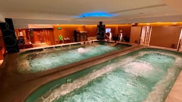A large indoor swimming pool with multiple lanes, surrounded by a reception area and a bar.