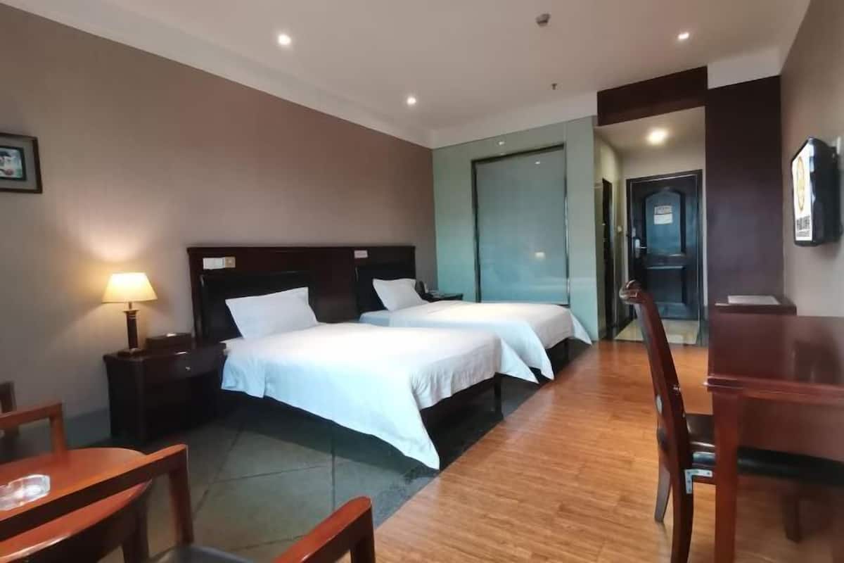 A hotel room with two beds, a desk, a chair, and a small table.
