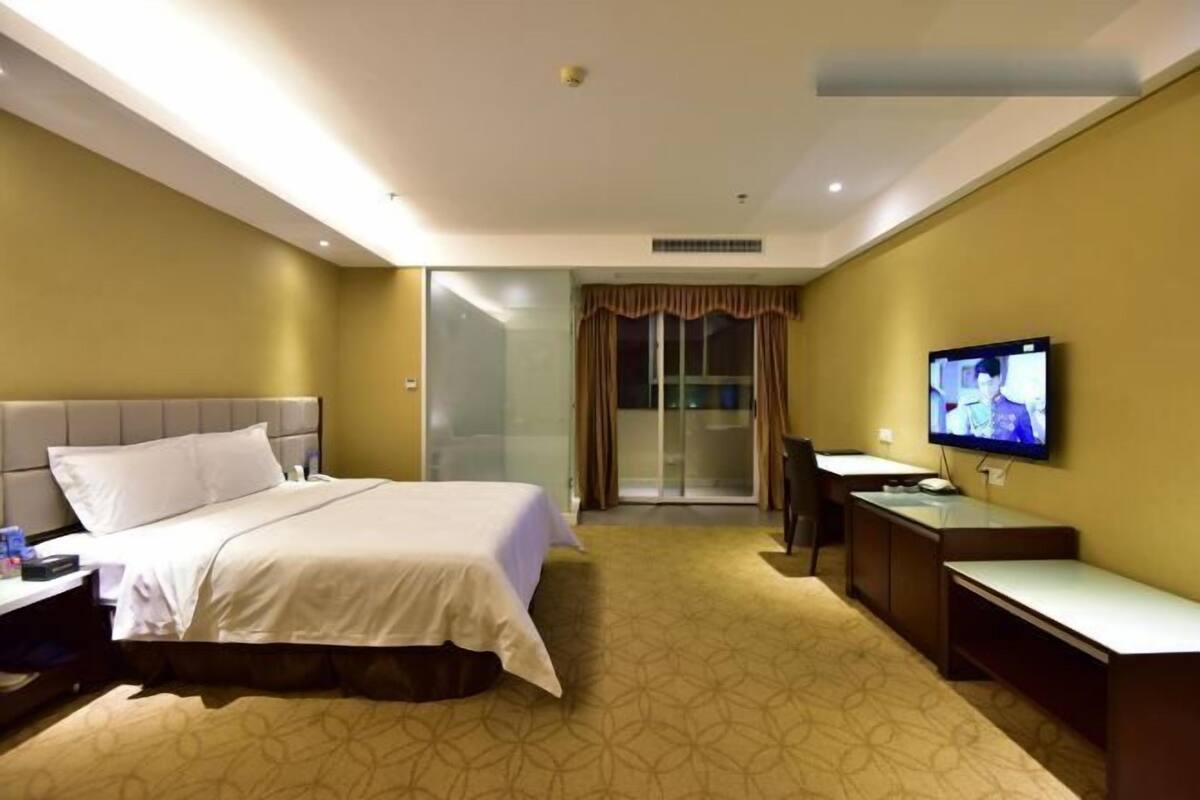 A hotel room with a bed, a desk, a television, and a sliding door leading to a balcony.