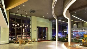 A modern hotel lobby with a curved reception desk, seating area, and large windows. - Huasheng Holiday Hotel (Kaiping)