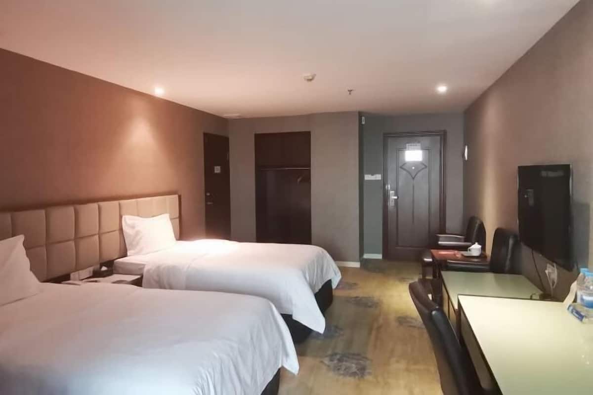 A hotel room with two beds, a desk, a television, and a door.