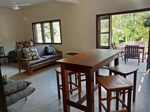Relax in a cozy living area with a dining table, sofa, and chairs, offering a view of lush greenery.