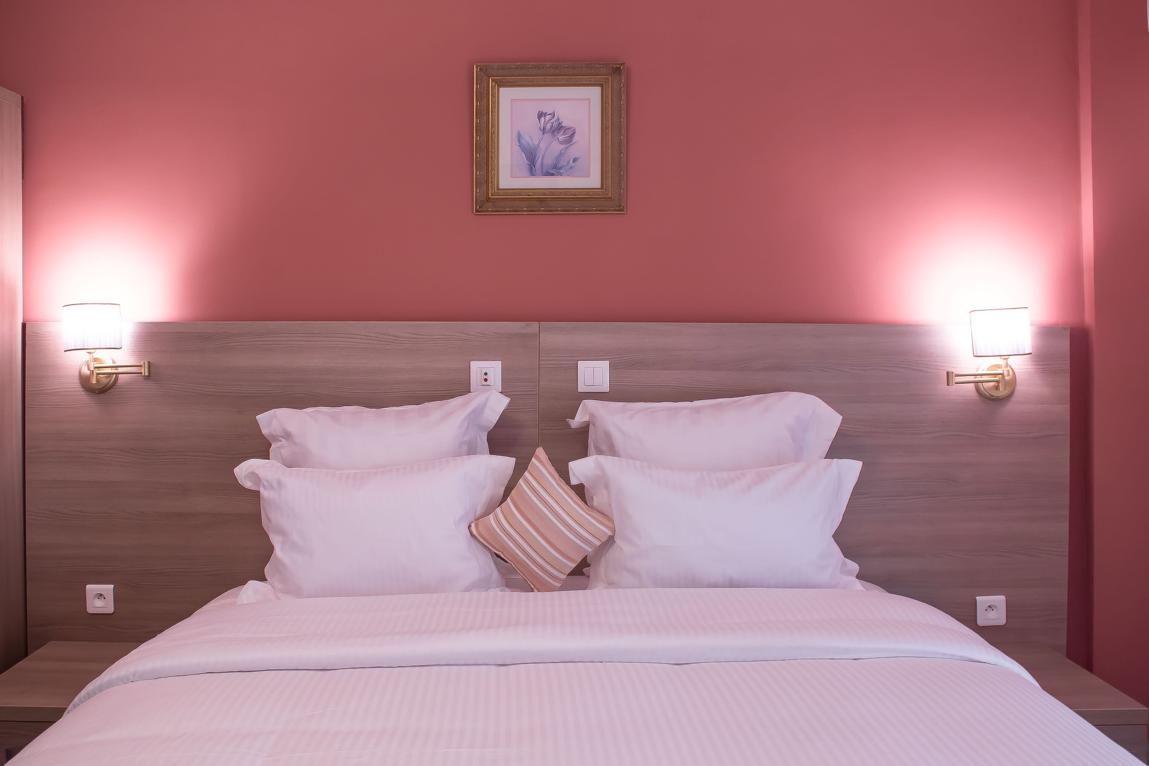A neatly made bed with white linens and striped pillows, a wooden headboard, and two wall-mounted reading lamps.