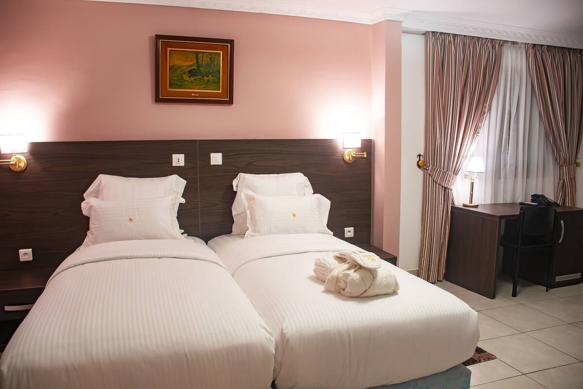 A hotel room with two beds, a desk, a chair, a framed picture on the wall, and curtains.