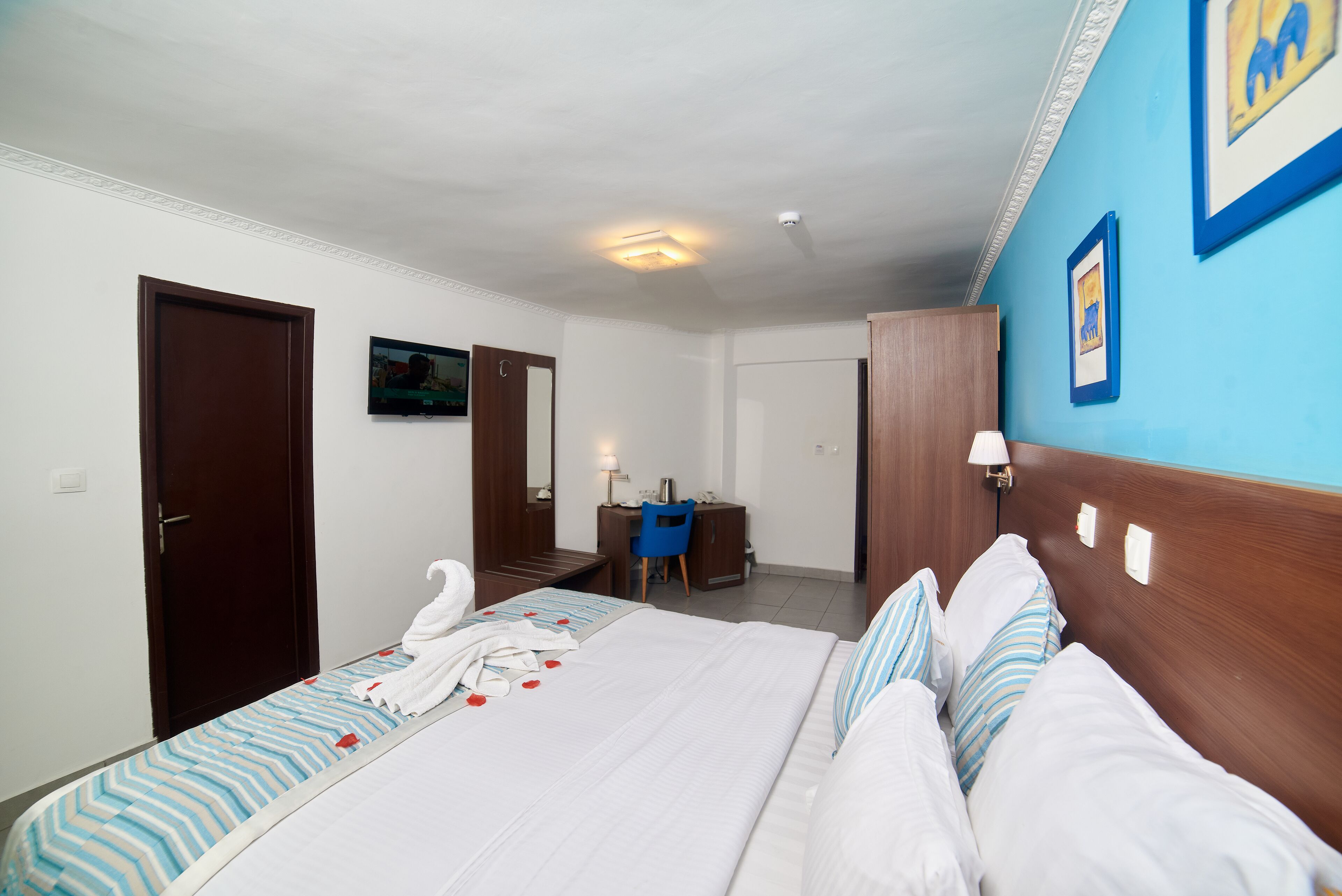 A hotel room with a large bed, a desk, a chair, and a blue wall with framed pictures.