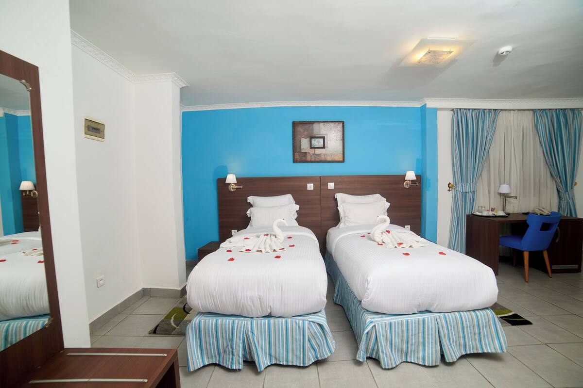 A hotel room with two beds, a desk, a chair, and a mirror.