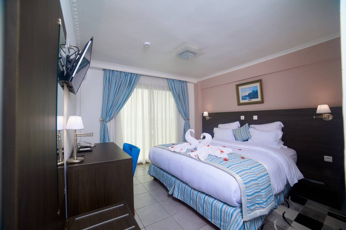 A hotel room with a bed, a desk, a chair, a TV, and a window with curtains.