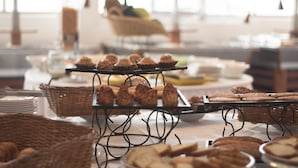A buffet table with various baked goods and pastries, including muffins and cookies, arranged on metal stands and wicker baskets.