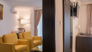 A hotel room with a yellow armchair, a desk with a lamp, a mirror, and a wardrobe.
