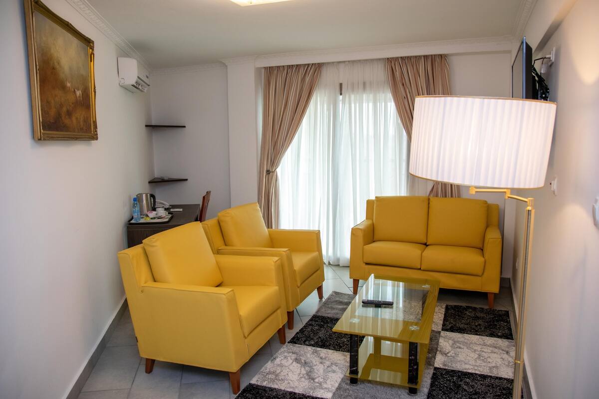 A living room with two yellow armchairs, a glass coffee table, a lamp, and a painting on the wall.