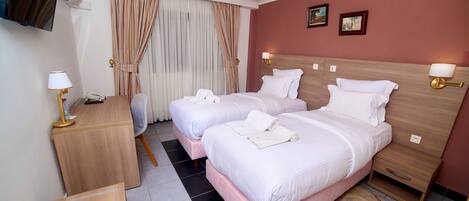 A hotel room with two beds, a desk, a chair, a TV, and a window with curtains.