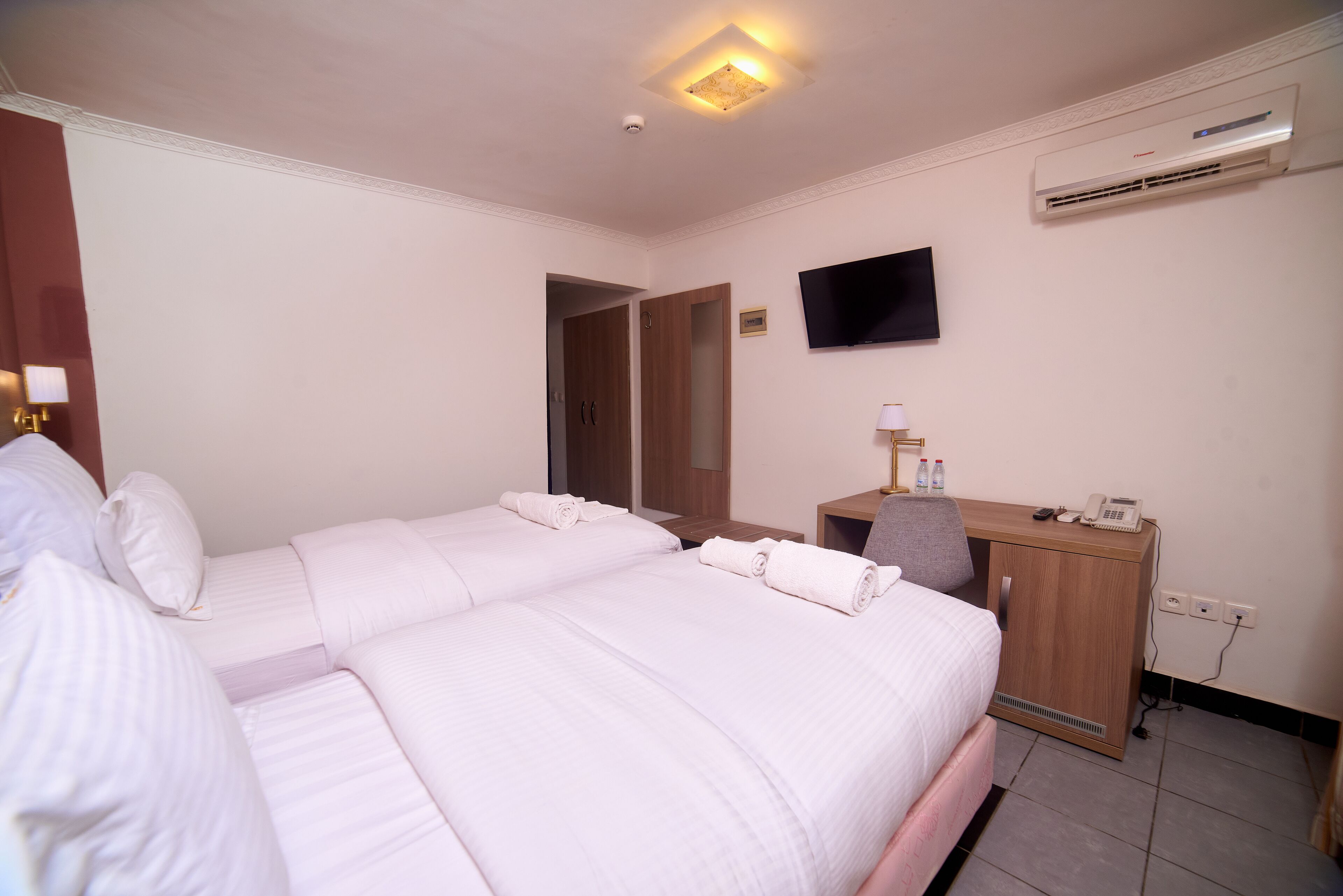 Habitación de hotel con dos camas, un escritorio, un televisor de pantalla plana, un equipo de aire acondicionado y una puerta que da a otra habitación.