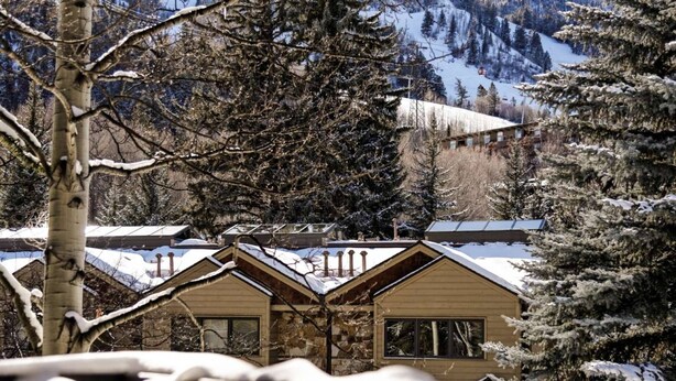 Une cabane à la façade en pierre, dotée de nombreuses fenêtres et dont le toit est recouvert de neige.