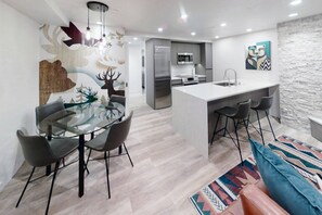 Une cuisine moderne dotée d’un îlot central, un coin repas avec une table en verre et un espace de vie comprenant un canapé et un tapis à motifs.