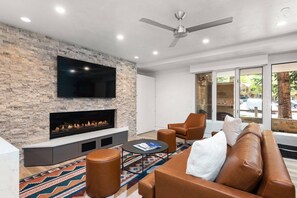 A modern living room with a stone wall, a flat-screen TV, a fireplace, leather furniture, and a large window with a view of the outdoors. - Remodeled With Luxury Finishes. Easy Walk to Aspen Mtn. Full Kitchen, Gas FP, W/D. Free Parking (Aspen)