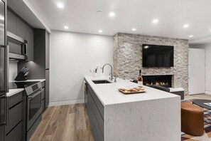 Une cuisine moderne avec un mur d’accent en pierre, un téléviseur encastré et une cheminée.