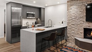Une cuisine moderne dotée d’un îlot central, de tabourets de bar, d’un mur décoratif en pierre et d’une cheminée.