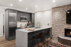 A modern kitchen with a central island, bar stools, a stone accent wall, and a fireplace.