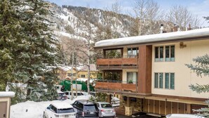 Un bâtiment à deux étages doté d’un balcon, entouré d’arbres couverts de neige et de voitures garées.