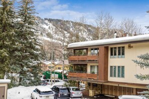 Un bâtiment à deux étages doté d’un balcon, entouré d’arbres couverts de neige et de voitures garées.