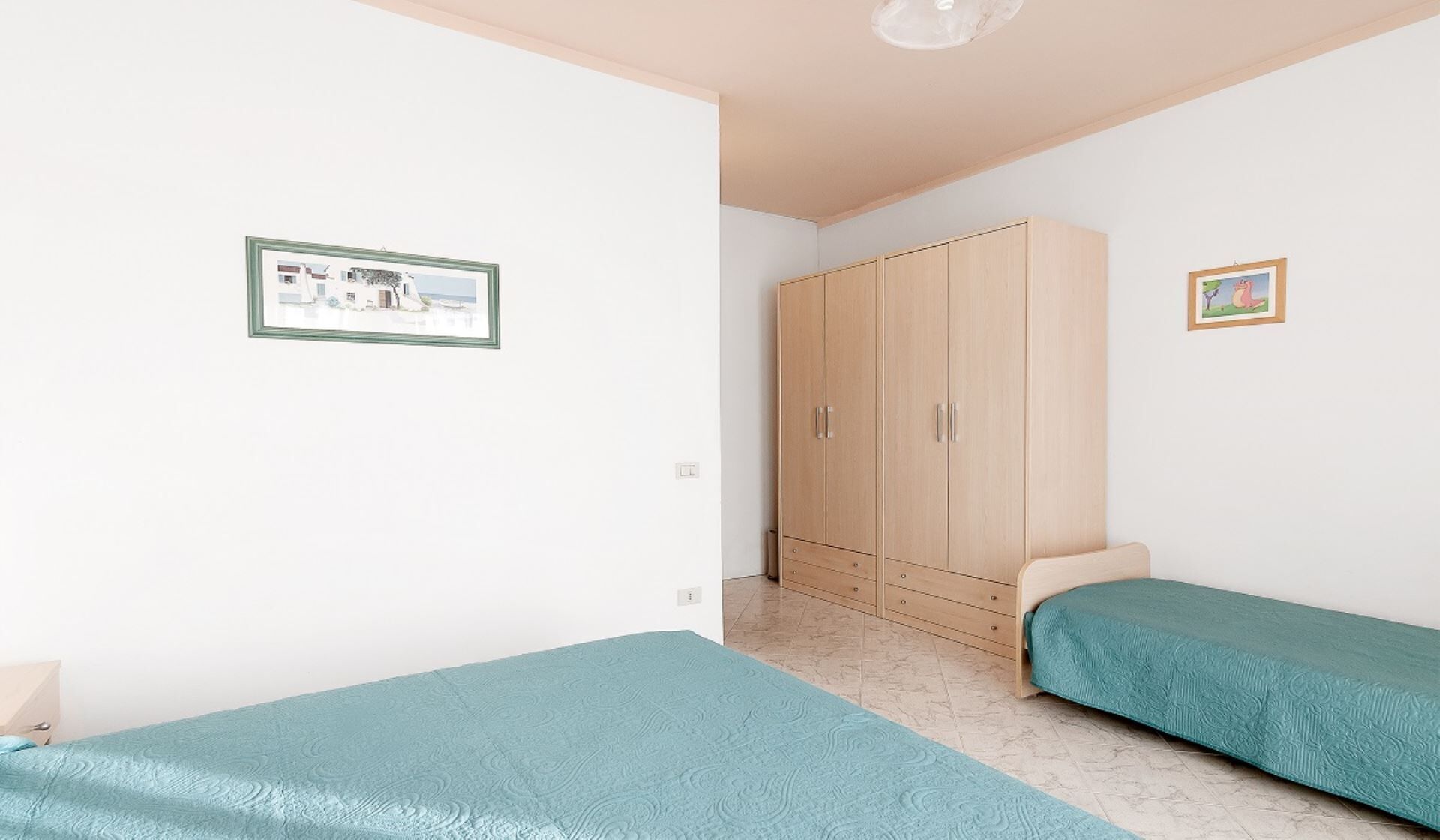 Ein Schlafzimmer mit zwei Einzelbetten, einem Kleiderschrank und zwei gerahmten Bildern an der Wand.