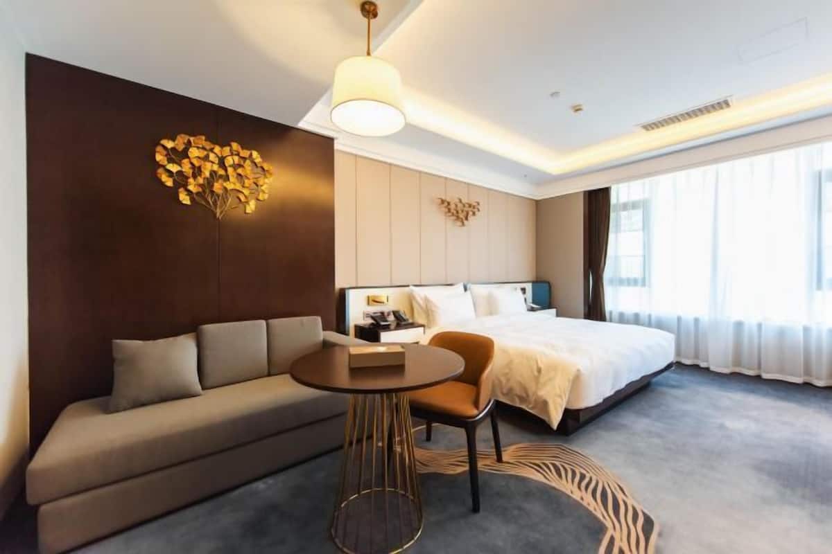 Habitació d'hotel moderna amb un llit gran, un sofà, una taula rodona petita i una decoració mural.