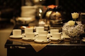 Una mesa con varias tazas y platillos blancos, un florero con flores blancas y una tetera al fondo.