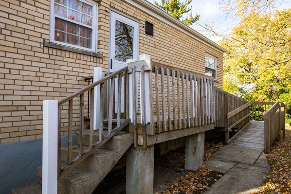 A brick house with a wooden deck and a concrete staircase leading to a porch.
