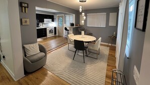 A modern kitchen with dark cabinets, a white stove, and a microwave. There is a dining area with a round table and chairs, and a gray sofa with a striped cushion. - Cozy, Modern Escape; PlayStation 5 and King Suite (Cincinnati)