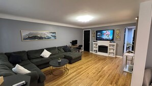 A modern living room with a sectional sofa, a fireplace, a flat-screen TV, and a wooden floor. - Cozy, Modern Escape; PlayStation 5 and King Suite (Cincinnati)