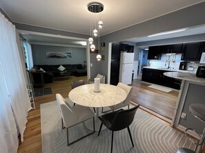 A modern kitchen with a marble island, black cabinets, and a dining area with a round table and chairs.