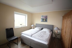 Una camera da letto con un letto, una sedia, una finestra, una lampada e un quadro appeso al muro.