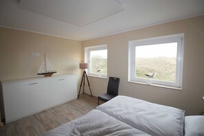 A bedroom with two beds, a desk, a chair, and two windows.