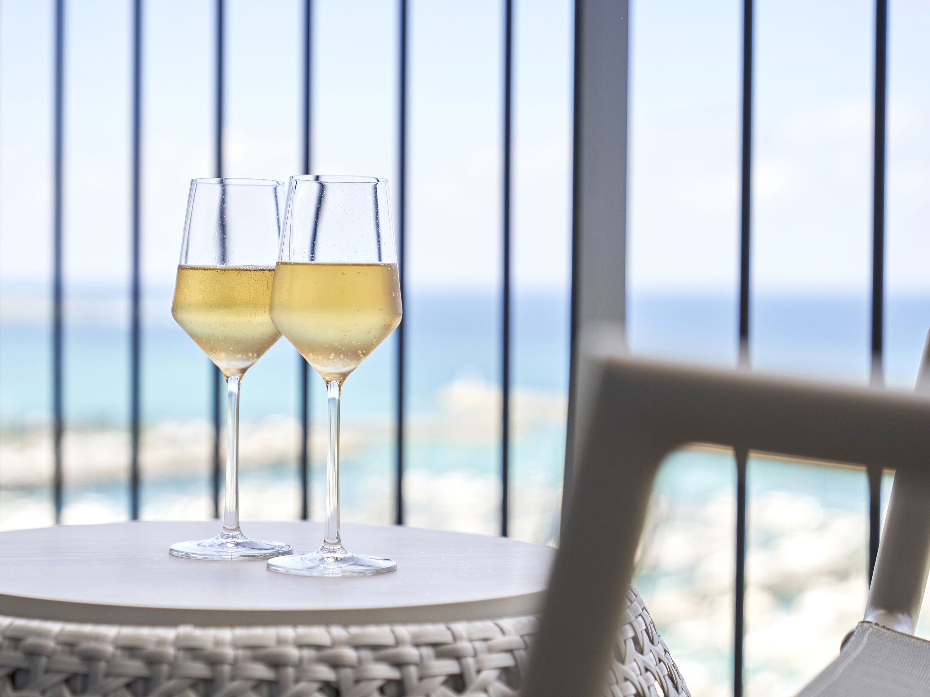 Two glasses of white wine on a round table with a view of the ocean.