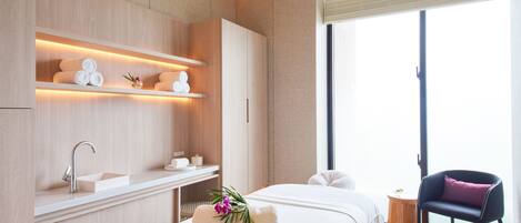 Una habitación de hotel moderna con una cama grande, una mesita de noche, un estante empotrado con toallas, una pequeña mesa redonda y una silla.