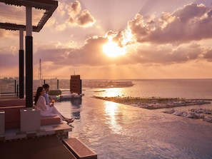 Una piscina en la azotea con vistas al mar y al paisaje urbano durante el atardecer.
