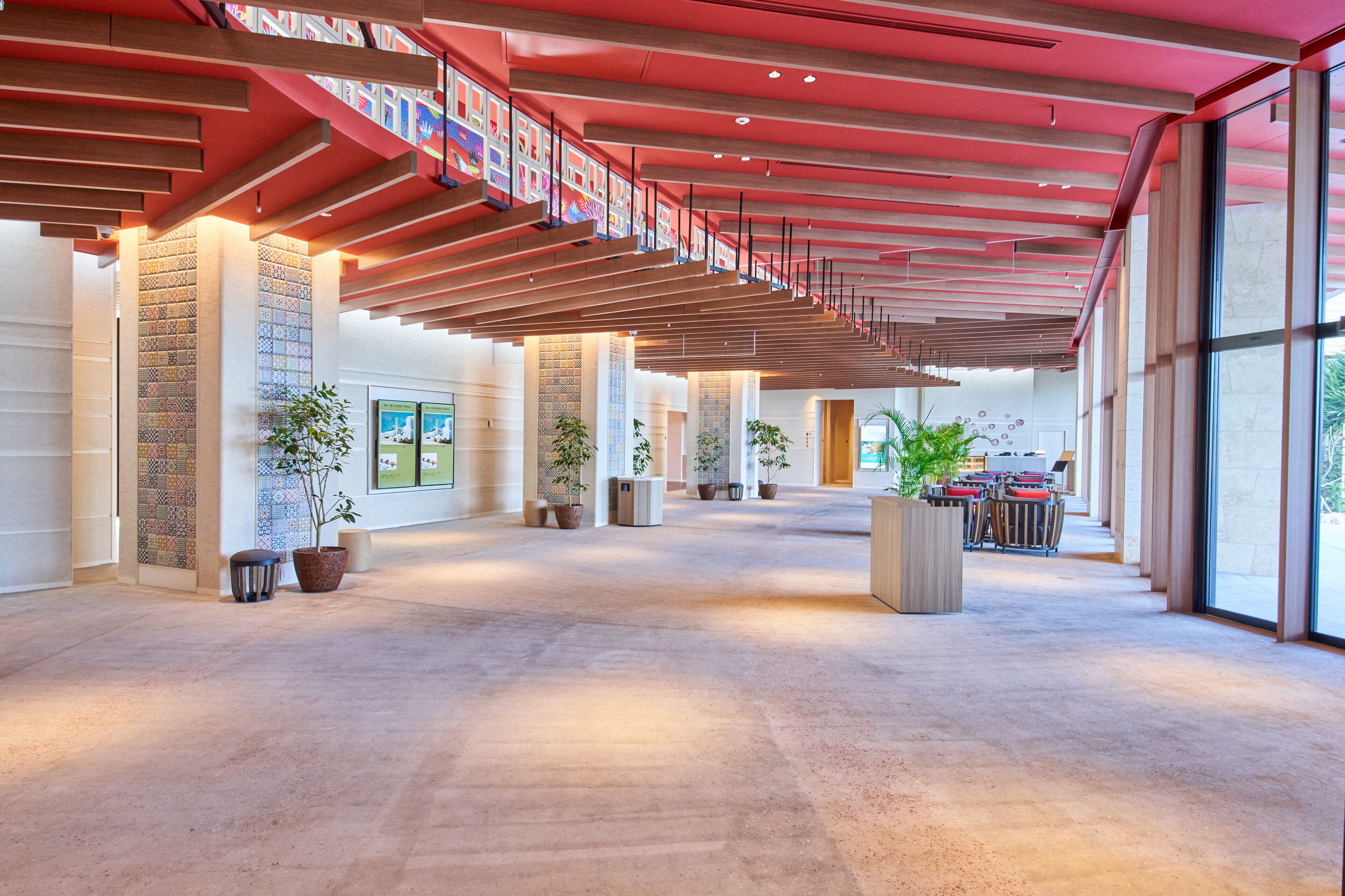 A spacious lobby with a high ceiling, large windows, and potted plants.