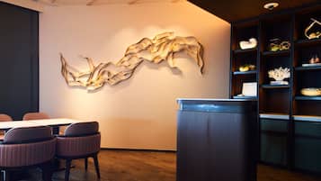 A modern interior with a wooden floor, a reception desk, a seating area with chairs, and a wall-mounted abstract art piece.