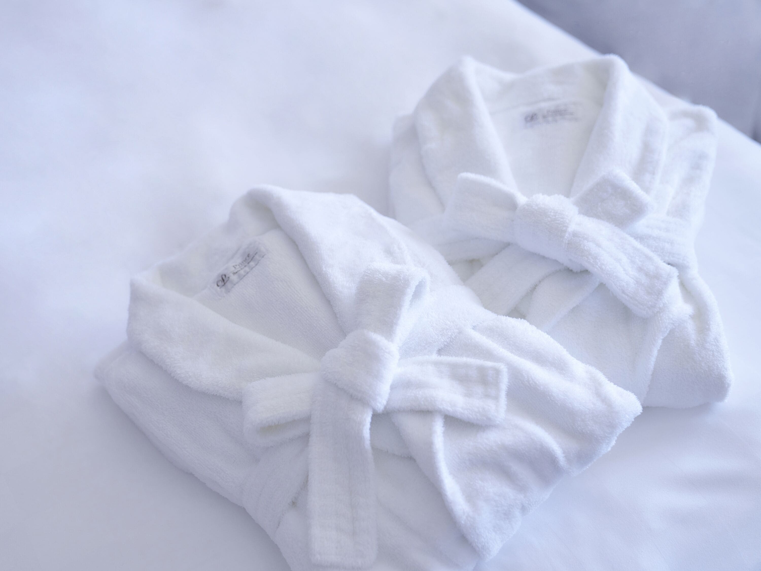 Two white bathrobes tied with a bow on a white pillow.