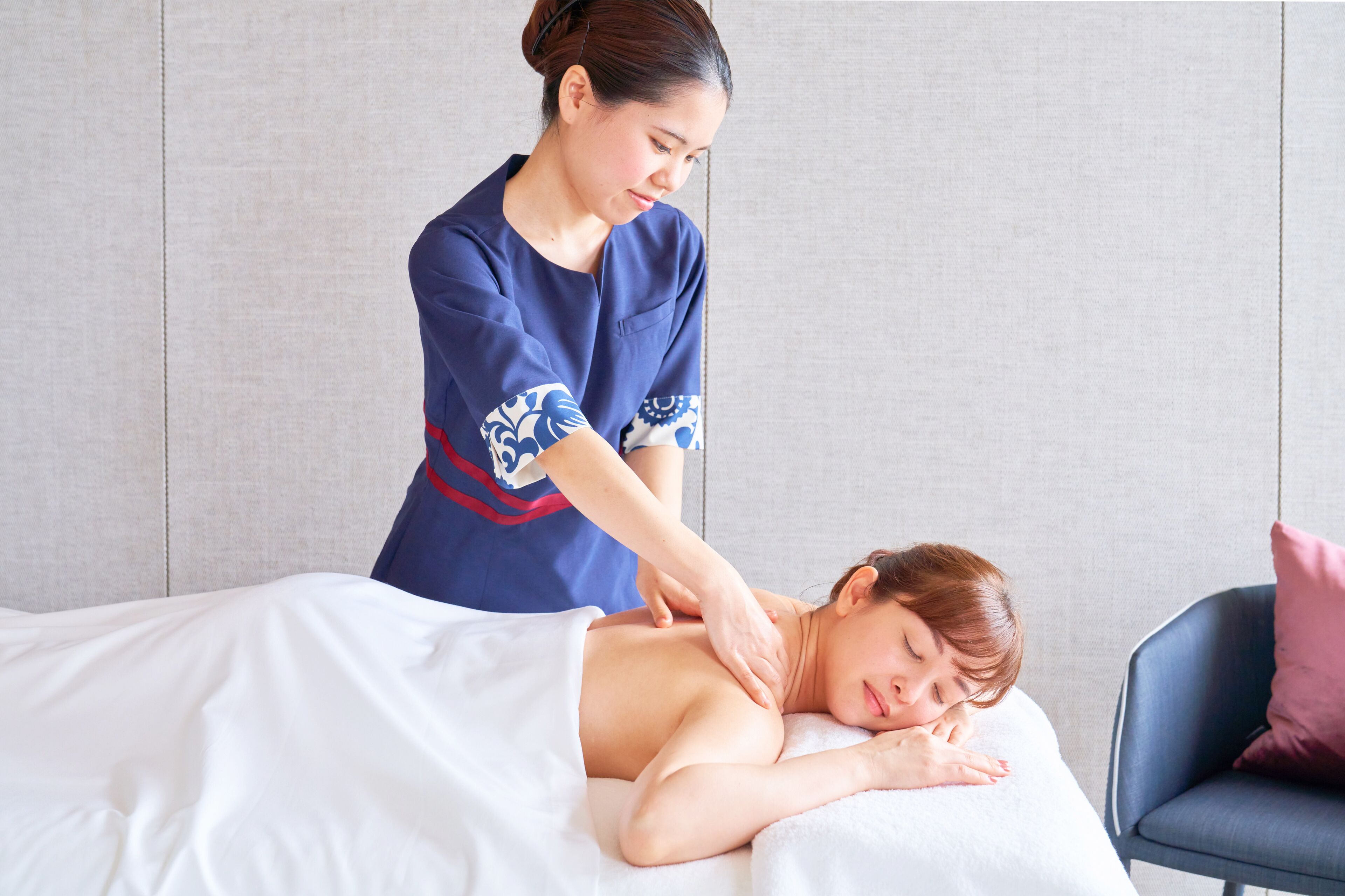 Une séance de massage effectuée dans une pièce équipée d’un lit, d’une table de massage et d’une chaise.