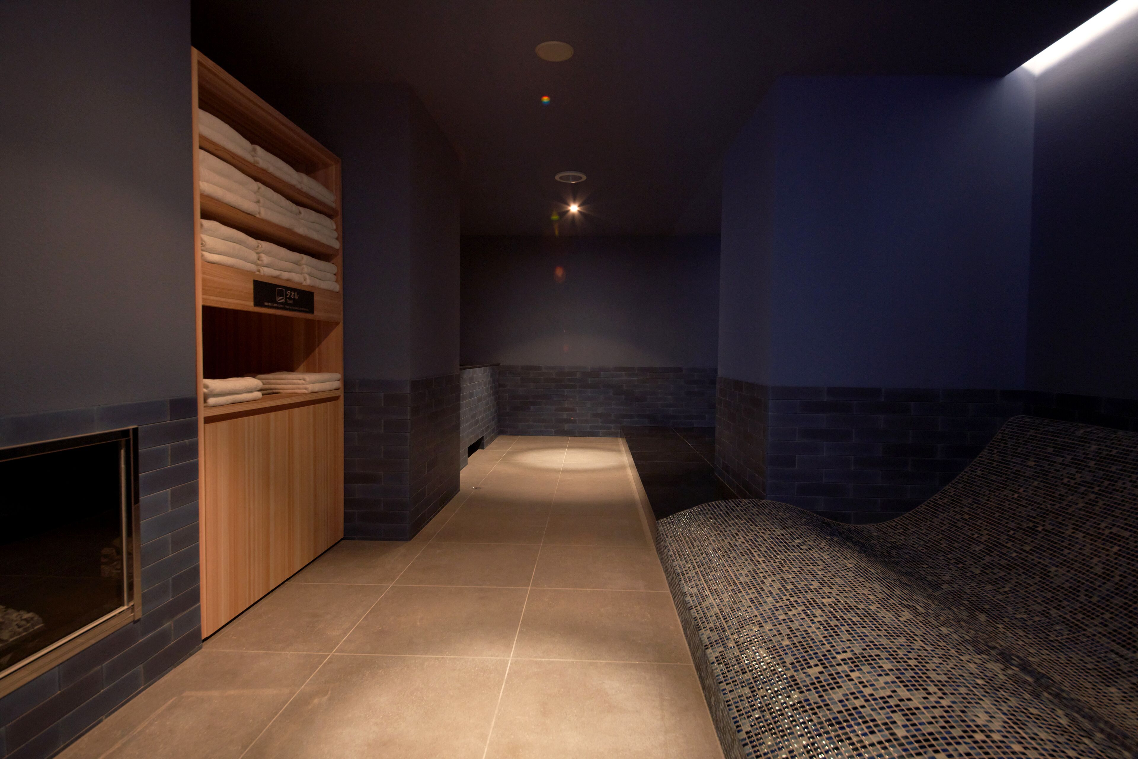 Un espacio de spa con un banco de madera, un perchero y suelo de baldosas.