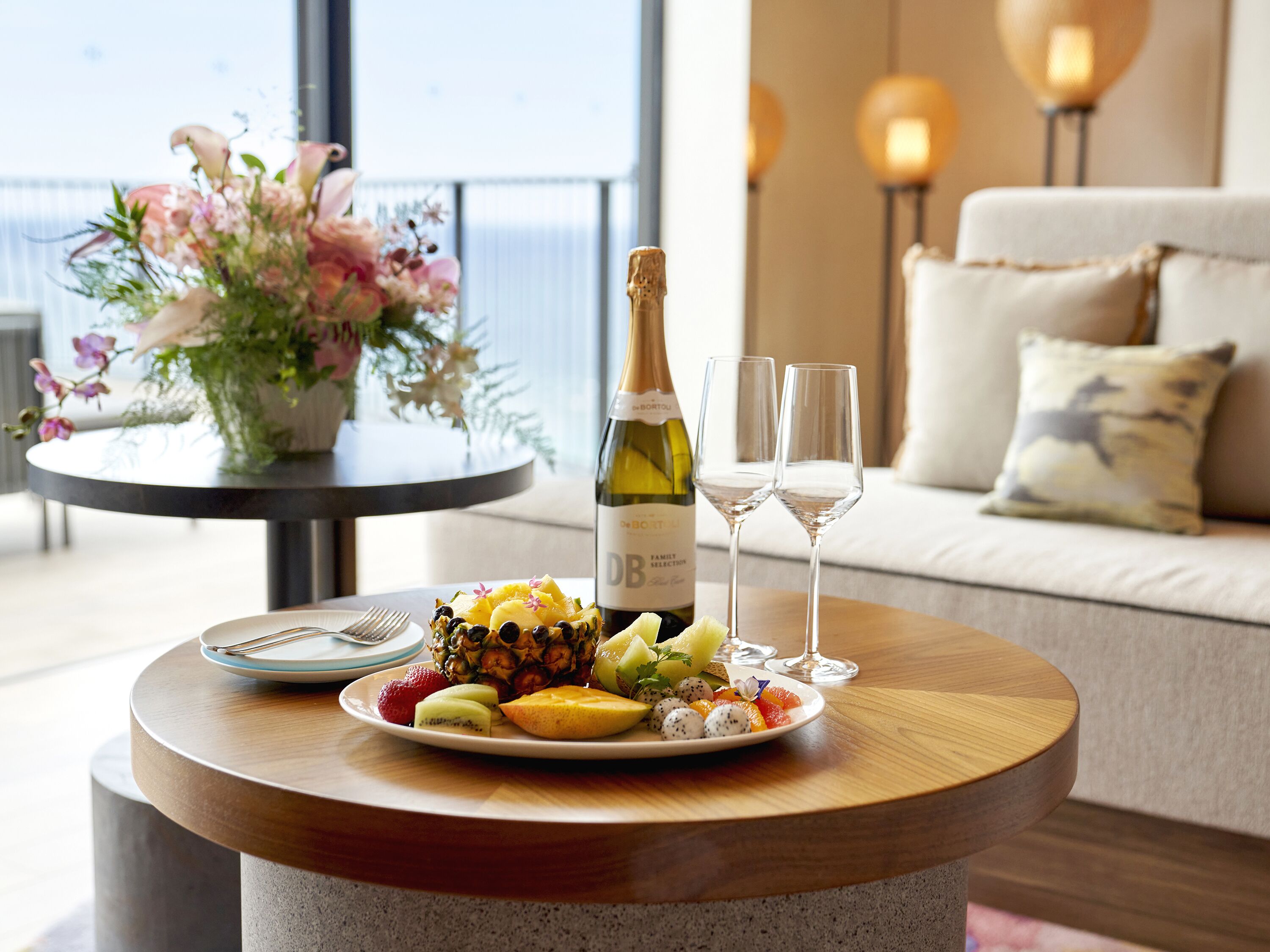 A table with a bottle of wine, two glasses, and a fruit platter.