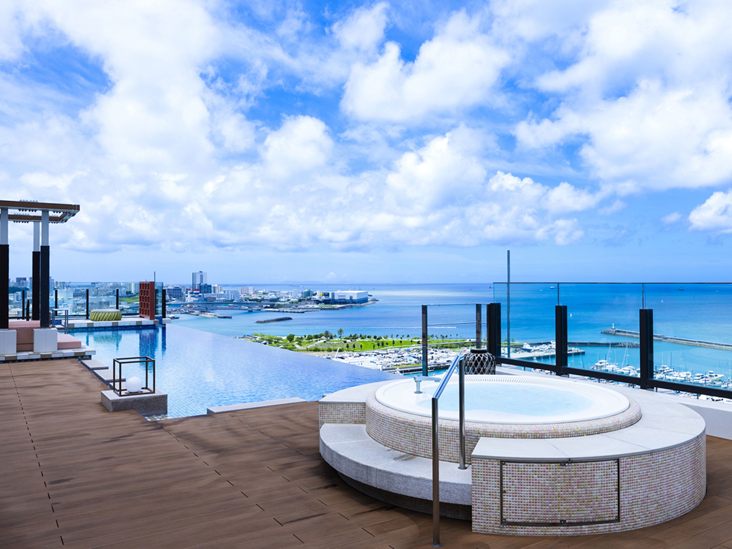 A rooftop infinity pool with a hot tub, overlooking a marina and cityscape.