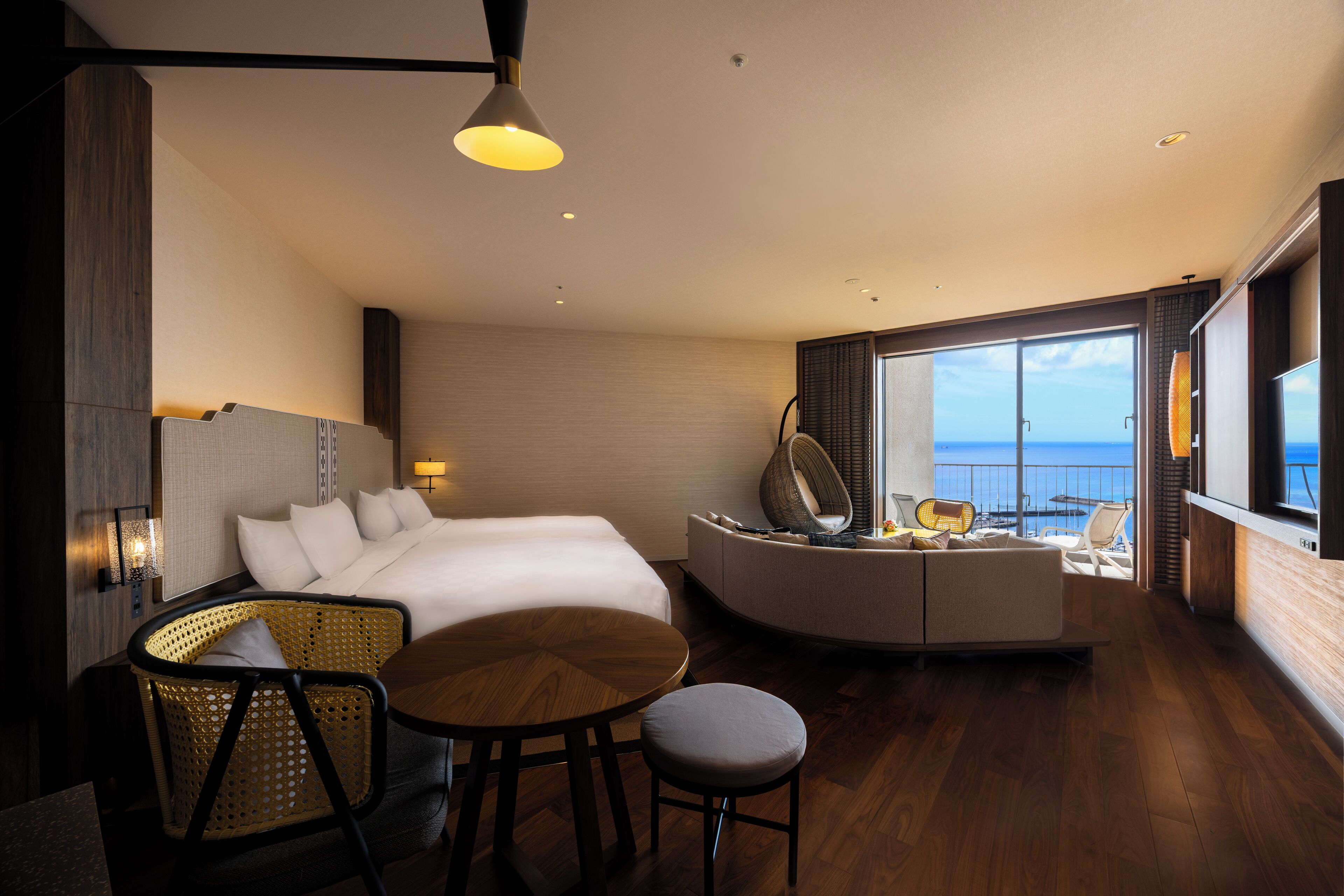 A modern hotel room with a bed, seating area, and a view of the sea.